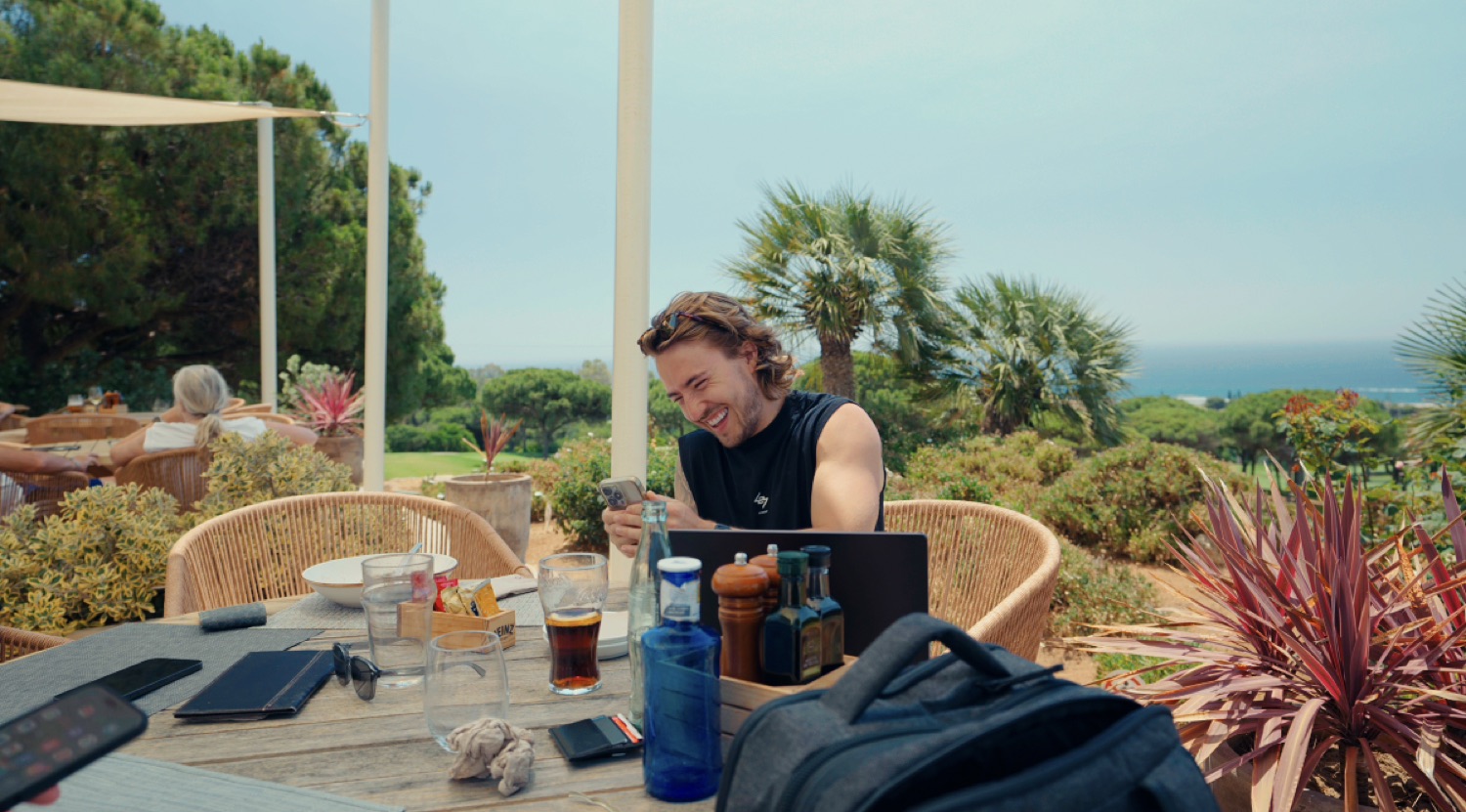 Tim working on a laptop at an outdoor table by the sea